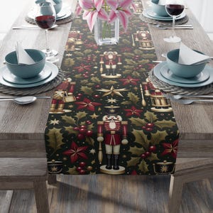Peut inclure: Une nappe de table sur le thème de Noël avec un fond sombre, présentant un motif répété de casse-noisettes, d'étoiles, de feuilles de houx et de baies en rouge, or et vert. La nappe est posée sur une table en bois avec des couverts et un vase de fleurs roses.