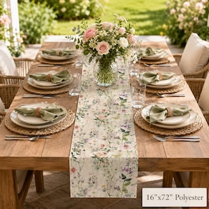 May include: A 16-inch by 72-inch polyester table runner featuring a botanical print of wildflowers in soft pastel colors. The runner is displayed on a wooden dining table set with woven placemats, white plates, and green napkins.