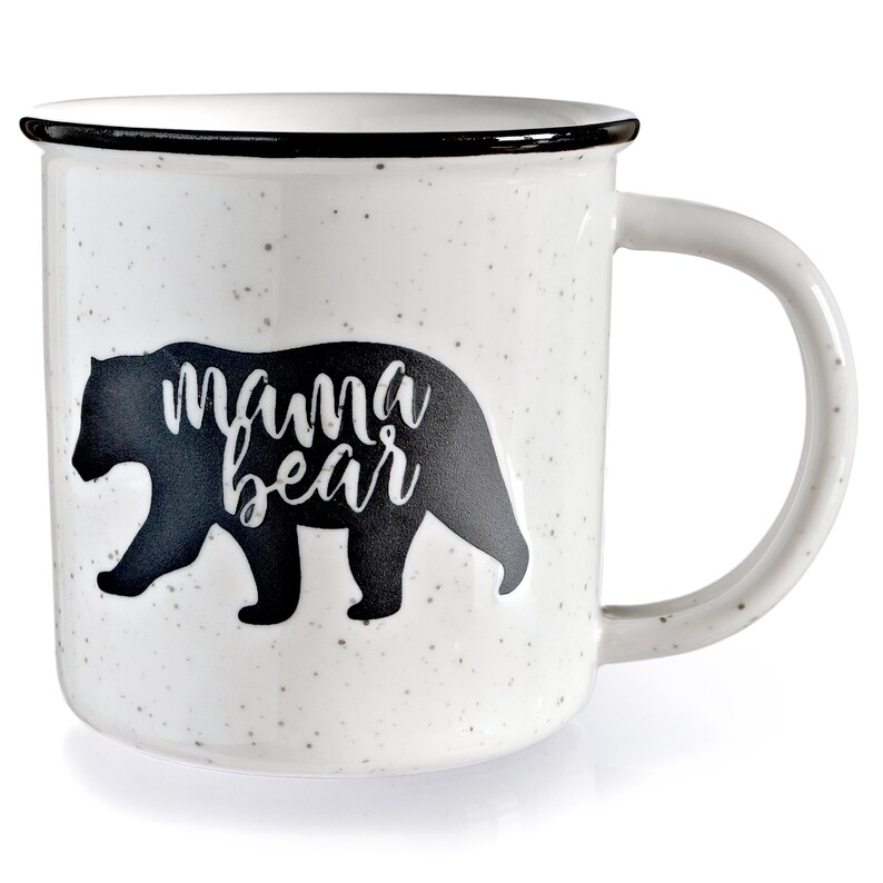 May include: White ceramic mug with a black silhouette of a bear and the text "mama bear" printed on it. The mug has a black rim and a speckled finish.