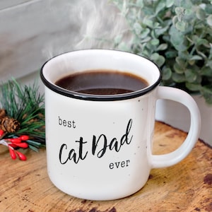 Pode incluir: Caneca de cer&acirc;mica branca com texto preto que diz "best cat dad ever". A caneca est&aacute; cheia de caf&eacute; e vapor est&aacute; subindo do topo.