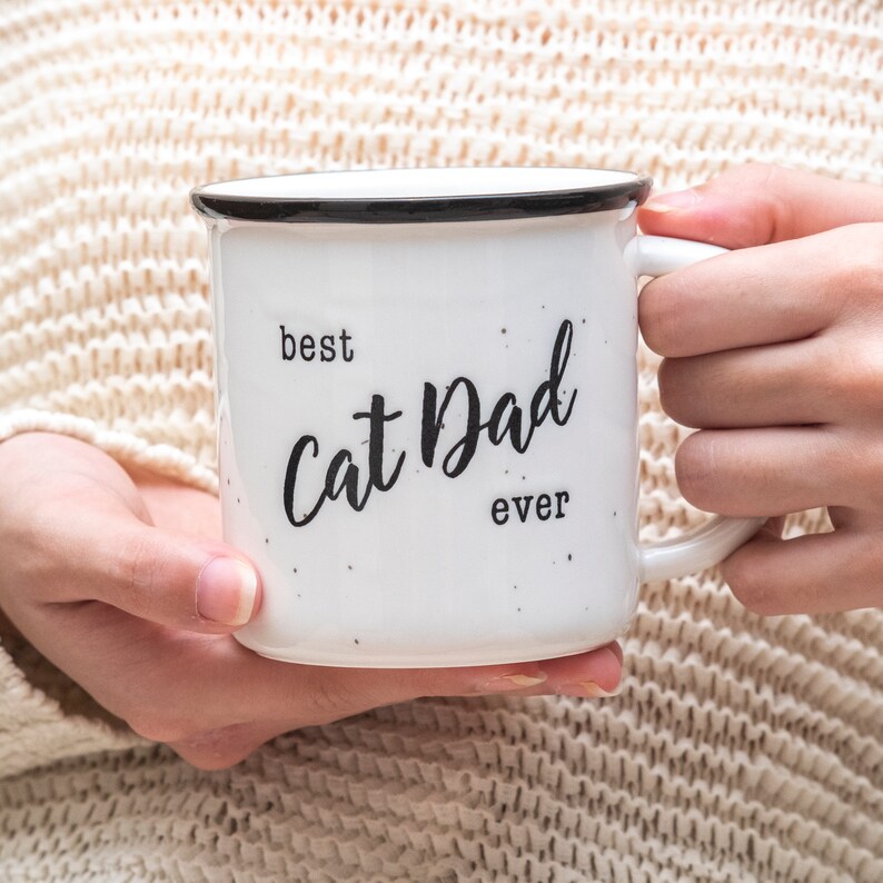Pode incluir: Caneca de cer&acirc;mica branca com borda e al&ccedil;a pretas. A caneca tem texto preto que diz "best cat dad ever".
