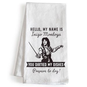 May include: White kitchen towel with the text "HELLO, MY NAME IS Inigo Montoya" and a black and white illustration of a man holding a sword. Below the illustration is the text "YOU DIRTIED MY DISHES Prepare to dry!"