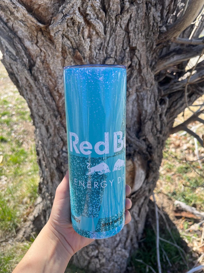 Peut inclure: Un gobelet turquoise bleu avec un logo Red Bull blanc et le texte "Energy Drink". Le gobelet a une finition scintillante.