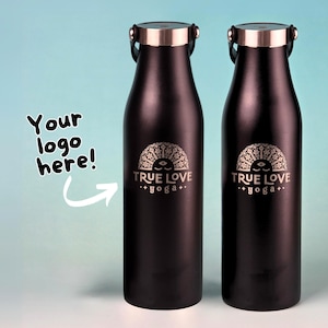 May include: Two dark brown metal water bottles with silver-toned caps. Each bottle features a laser-engraved design of a stylised sun with a face and the text "TRUE LOVE yoga". To the left, the text "Your logo here!" appears with an arrow.