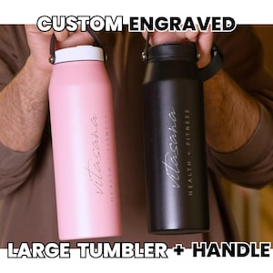Custom engraved large tumbler with handle. Stainless steel water bottle, pink and black, with 'Vitasana Health + Fitness' logo. Ideal for gym, travel, and daily hydration.
