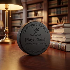 May include: A black hockey puck with the words "OBJECTION OVERRULED" and crossed hockey sticks and a gavel. Below the graphic is the text "[Player Name] Attorney at Law | Center Ice [Law Firm Name] Hockey Club."