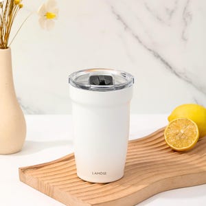 White stainless steel tumbler with clear lid, perfect for hot or cold beverages. Features Lamose branding. Includes sliced lemon on a wooden tray.