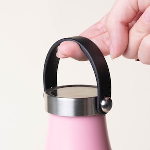 Peut inclure: Une bouteille d'eau en acier inoxydable rose avec une poignée en caoutchouc noir. La poignée a un bouton en plastique noir à l'extrémité.