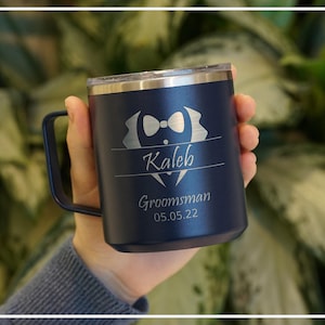 Personalized navy blue tumbler for a groomsman, featuring laser-engraved name Kaleb and Groomsman 05.05.22 with a bow tie design. Insulated, stainless steel mug for wedding parties.