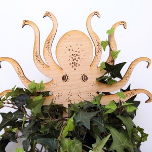 May include: A wooden cutout of an octopus with eight tentacles, the octopus is surrounded by green leafy plants.