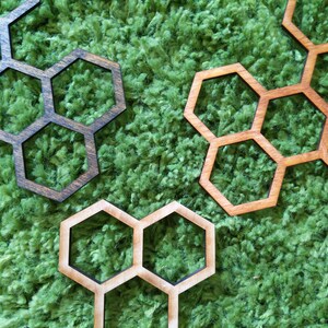 May include: Three wooden honeycomb-shaped coasters in different sizes. The coasters are brown, light brown, and dark brown. They are arranged on a green, fuzzy surface.