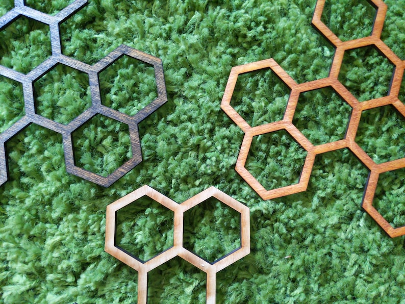 May include: Three wooden honeycomb-shaped coasters in different sizes. The coasters are brown, light brown, and dark brown. They are arranged on a green, fuzzy surface.