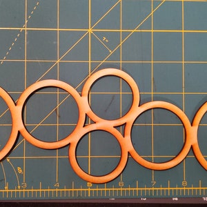 May include: Five wooden circles of varying sizes are arranged in a pattern on a green cutting mat. The circles are all the same color, a light orange-brown.