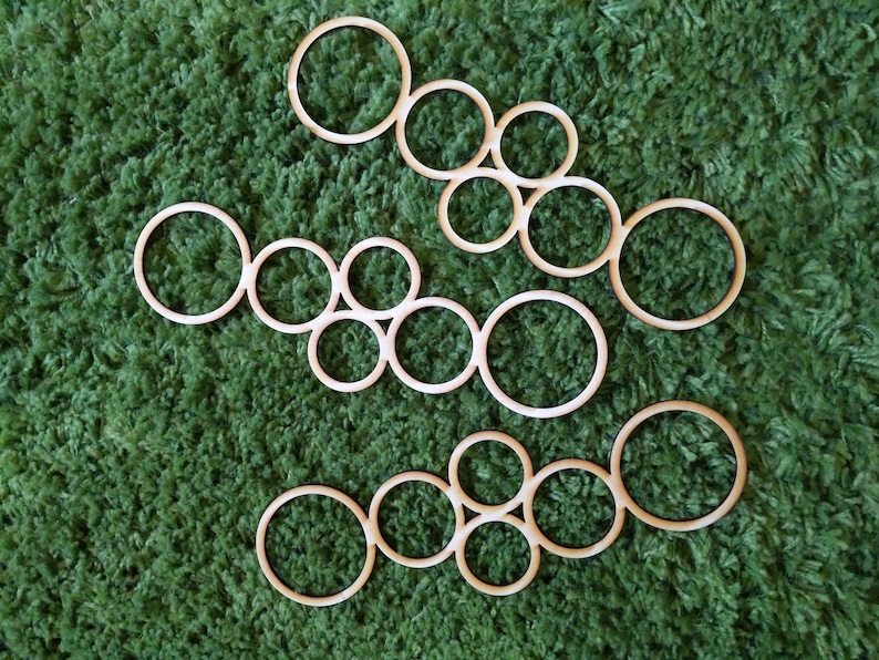 May include: A set of wooden circles of varying sizes, arranged in a pattern on a green carpet. The circles are all made of the same type of wood and have a natural finish.