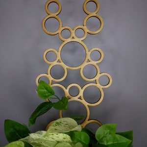 May include: A wooden plant stand with a geometric design of overlapping circles. The stand is made of natural wood and has a light brown color. The stand is decorated with green plants.