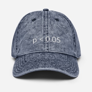 Könnte beinhalten: Eine Baseballkappe in Jeansblau mit gebogenem Schirm. Auf der Vorderseite ist der gestickte Text "p < 0,05" in Weiß zu sehen. Die Kappe hat einen Vintage-Look.