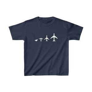 May include: Navy blue t-shirt featuring a white graphic of an airplane evolution, from paper airplane to jet. The design shows the progression of flight. A comfortable, casual tee for aviation enthusiasts.