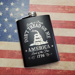 May include: Black metal flask with a silver engraving of a snake and the words "Don't Tread On Me", "Liberty or Death", "America", "Land of the Free", and "1776".