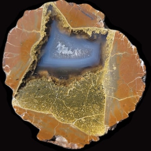 Peut inclure: Une tranche d'agate polie présentant une cavité centrale remplie de cristaux bleu clair translucides. La pierre environnante affiche des tons terreux orange rouille et jaune moutarde avec un réseau de fines veines blanches sur la surface.