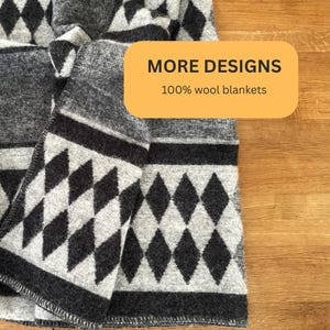 May include: A folded gray and white wool blanket with a geometric diamond pattern. The blanket has a dark gray border and features the text "MORE DESIGNS 100% wool blankets" in a yellow rectangle.
