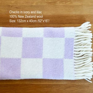 May include: A rectangular ivory and lilac checked blanket made of 100% New Zealand wool. The blanket measures 132cm long and 40cm wide. The edges have a fringe detail. The text "Checks in ivory and lilac" is visible.