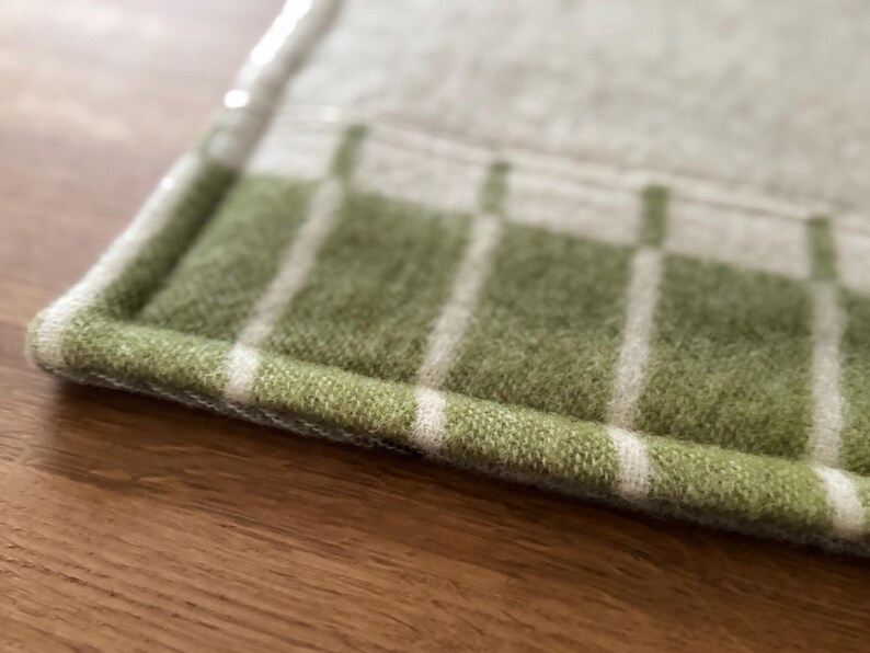 K&ouml;nnte beinhalten: Nahaufnahme eines gr&uuml;n-wei&szlig; karierten Textils. Das Textil hat ein weiches, strukturiertes Aussehen mit einer gr&uuml;nen Basis und wei&szlig;en vertikalen Streifen. Die Kanten sind sauber mit einem wei&szlig;en Rand versehen. Der Artikel ist wahrscheinlich ein K&uuml;chen- oder Wohnaccessoire.
