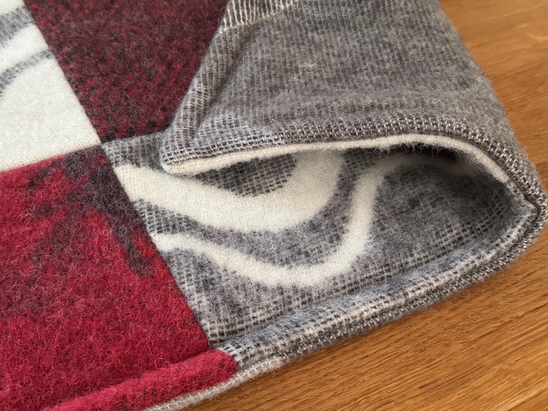 Close-up texture of the rich, deep maroon/red wool square on the checkered pet mat.