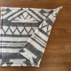 Close-up showing the folded edge and texture of the grey and white geometric patterned 100% wool mat.