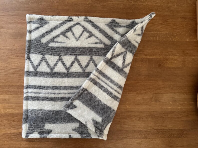 Close-up showing the folded edge and texture of the grey and white geometric patterned 100% wool mat.
