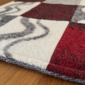 Checkered 100% wool pet mat, measuring 55x67cm, featuring deep maroon, white, and grey squares, some with wavy pattern. Size clearly marked.
