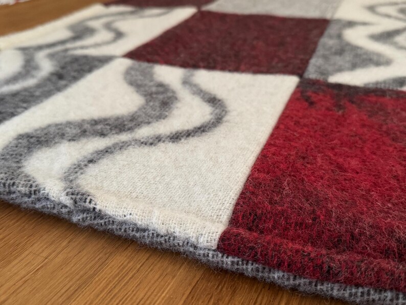 Checkered 100% wool pet mat, measuring 55x67cm, featuring deep maroon, white, and grey squares, some with wavy pattern. Size clearly marked.
