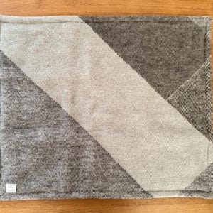 Top view of the checkered red, white, and grey 100% wool pet mat on a white background.
