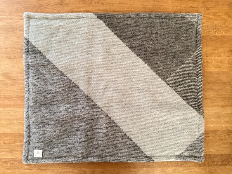 Top view of the checkered red, white, and grey 100% wool pet mat on a white background.