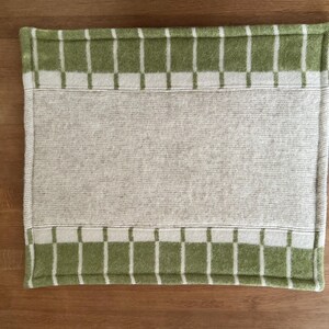 K&ouml;nnte beinhalten: Ein rechteckiger Tischset in heller Farbe mit einem gr&uuml;n-wei&szlig; karierten Rand. Die Mitte ist einfarbig hell. Der Tischset besteht aus einem weichen, gewebten Material.
