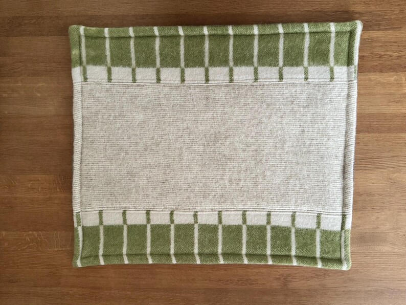 K&ouml;nnte beinhalten: Ein rechteckiger Tischset in heller Farbe mit einem gr&uuml;n-wei&szlig; karierten Rand. Die Mitte ist einfarbig hell. Der Tischset besteht aus einem weichen, gewebten Material.