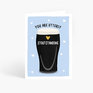 May include: A blue card with a white border and white hearts. The card features a black and white illustration of a glass of stout beer with a gold heart on the side. The text "You are utterly stoutstanding" is written in black on the card.
