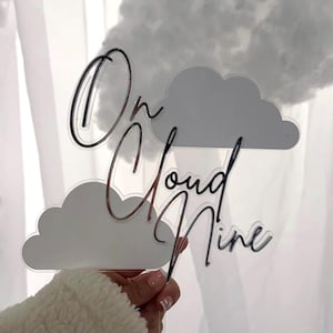 May include: White acrylic cake topper with two clouds and the text "On Cloud Nine" in black script.
