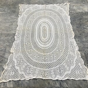 May include: White crocheted tablecloth with a large oval design in the center. The tablecloth has a delicate lace pattern.