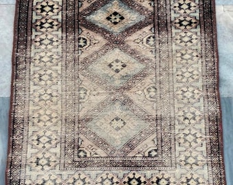 Puede incluir: Una alfombra vintage de color marrón y crema. La alfombra tiene un patrón geométrico con una forma de diamante central. La alfombra tiene un borde de flecos.