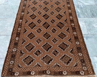 Puede incluir: Una alfombra de color marrón y blanco con un diseño geométrico. La alfombra tiene un borde con flecos.