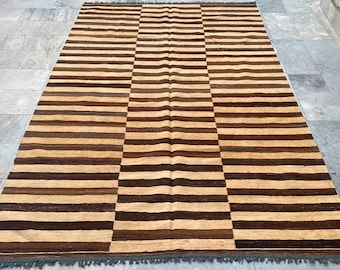 May include: A brown and beige striped rug with a subtle wave pattern. The rug has a fringe border.