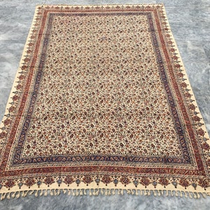 Könnte beinhalten: Eine cremefarbene Baumwolltischdecke mit einem Paisley-Druck in Rot-, Blau- und Brauntönen. Die Tischdecke hat einen Fransenrand und einen dekorativen Rand mit einem Paisley-Muster.