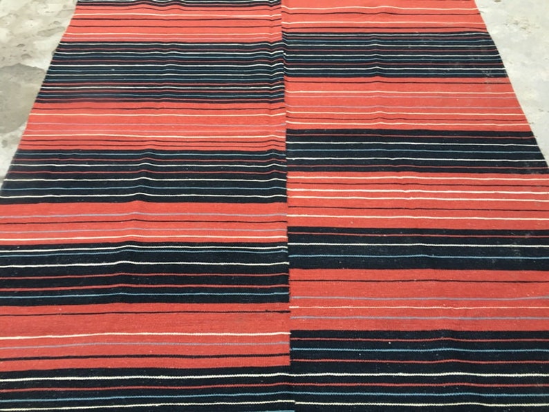 Pu&ograve; includere: Un tappeto a strisce rosse e nere con una trama tessuta. Il tappeto ha un motivo geometrico di strisce orizzontali.