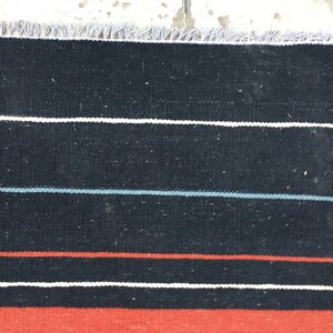 Pu&ograve; includere: Tappeto a strisce nere e rosse con accenti bianchi. Il tappeto ha un bordo con frange.