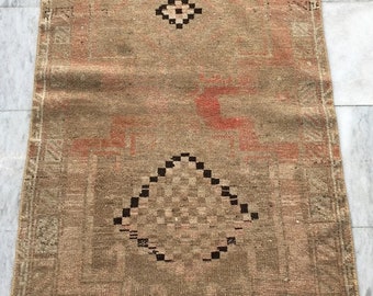 Puede incluir: Una alfombra vintage con fondo beige y un patrón geométrico en tonos marrones y rojos. La alfombra tiene un borde de flecos.