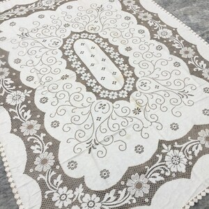Puede incluir: Mantel de mesa de crochet blanco con un delicado patrón floral y bordes festoneados.