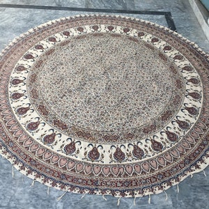 Könnte beinhalten: Eine runde, cremefarbene Tischdecke mit einem Paisley-Muster in Blau-, Rot- und Rosatönen. Die Tischdecke hat einen Fransenrand und ist aus Baumwolle.