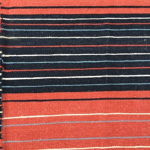 Pu&ograve; includere: Un primo piano di un tessuto tessuto con strisce alternate di rosso, bianco, nero e blu.