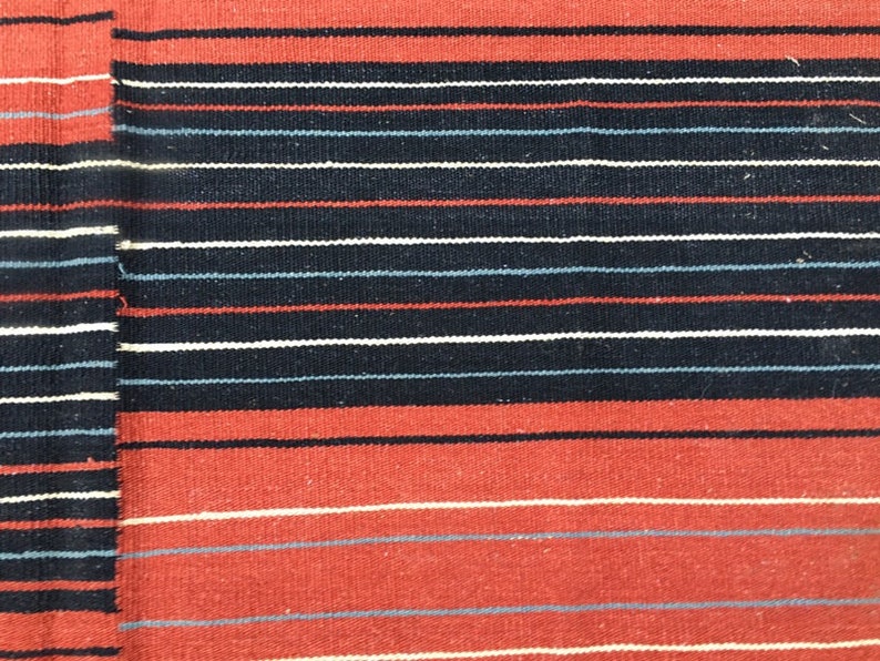 Pu&ograve; includere: Un primo piano di un tessuto tessuto con strisce alternate di rosso, bianco, nero e blu.