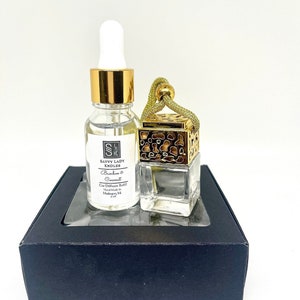 May include: A black box with a clear window containing a small glass bottle with a gold cap and a gold-coloured car air freshener with a brown and gold patterned top. The bottle and air freshener are labelled "Savvy Lady Candles Bamboo & Coconut Car Diffuser Refill Handmade in Malaysia 17 ml".